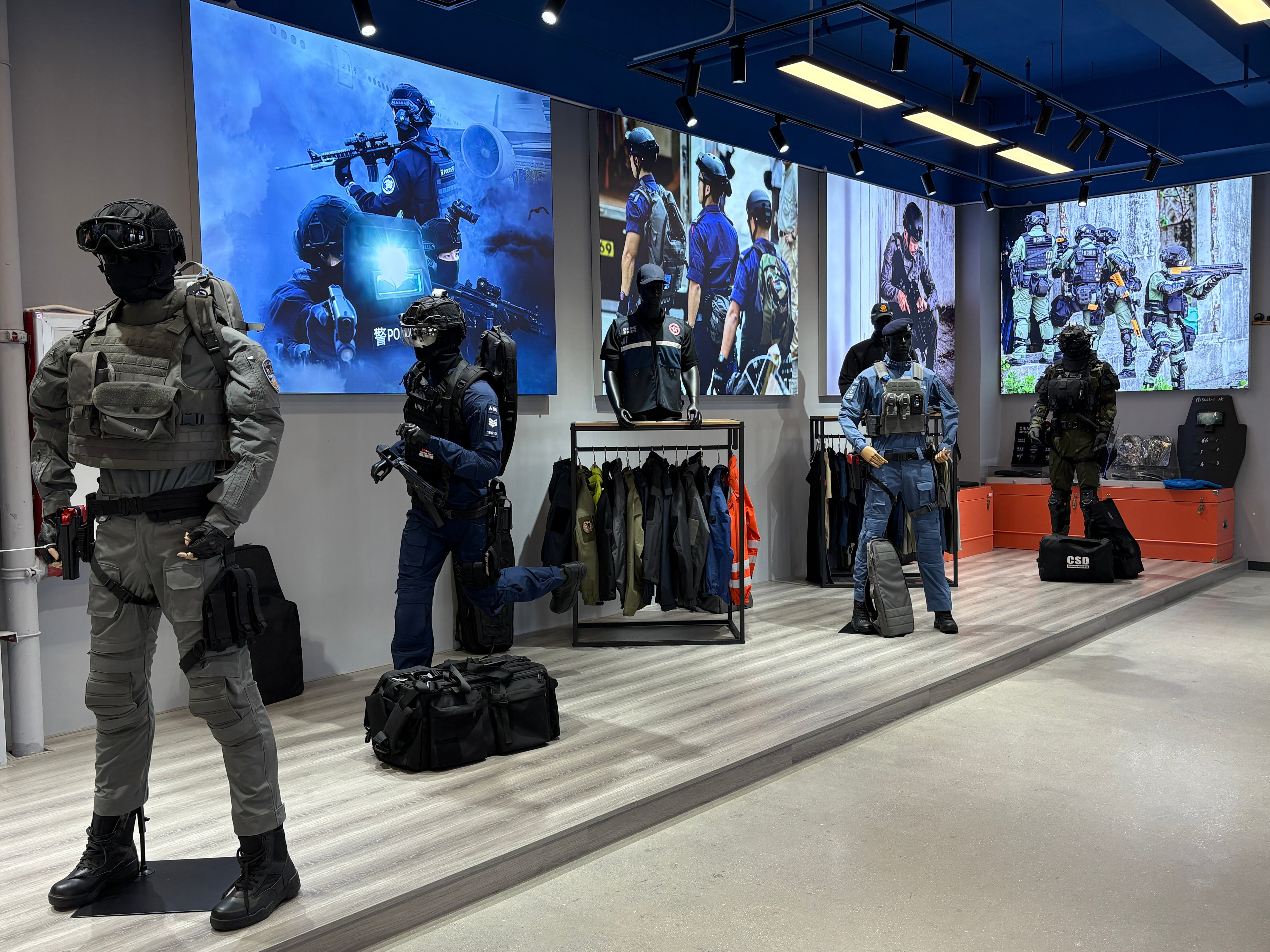 Display of tactical gear and uniforms in a showroom with large screens showing images of people in similar attire.